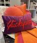 Preview: Kissen Glückspilz von Pad Home in lila mit orangefarbener Stickschrift, dekoriert mit weiteren Kissen in Orange und Pink